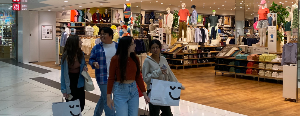 Four teenagers shopping at talking while walking past a clothing store.